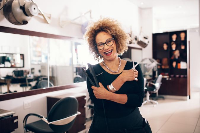 Joyful older woman hairdresser holding hair accessories