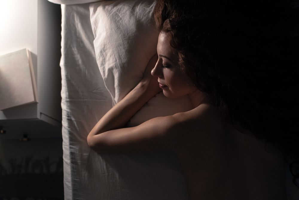 Back view of a naked woman lying down in bed
