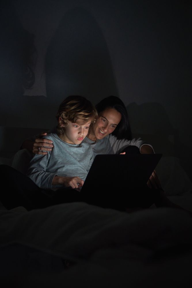 Woman with son using laptop while doing homework in darkness