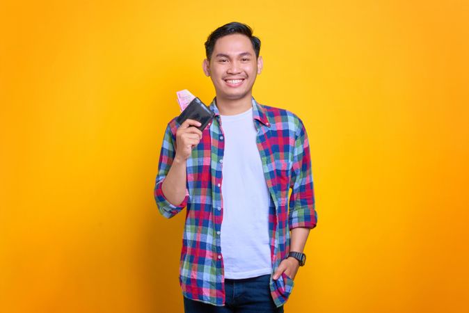 Smiling Asian man smiling while holding wallet with hand in his pocket