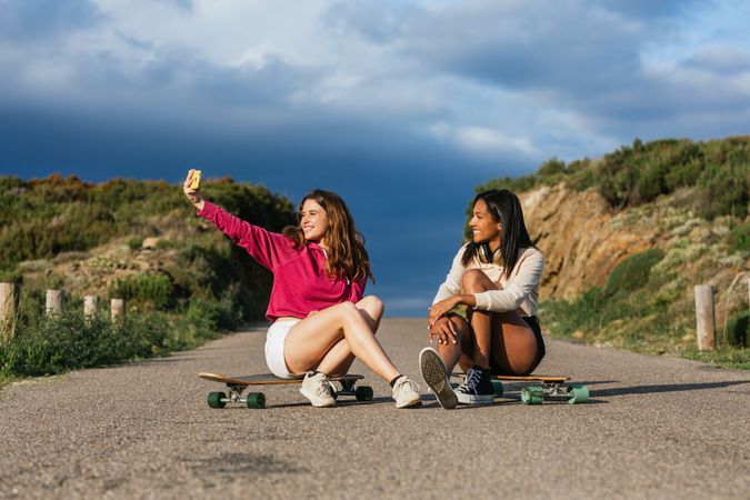 Cheerful multiethnic friends on longboards taking selfie on smartphone