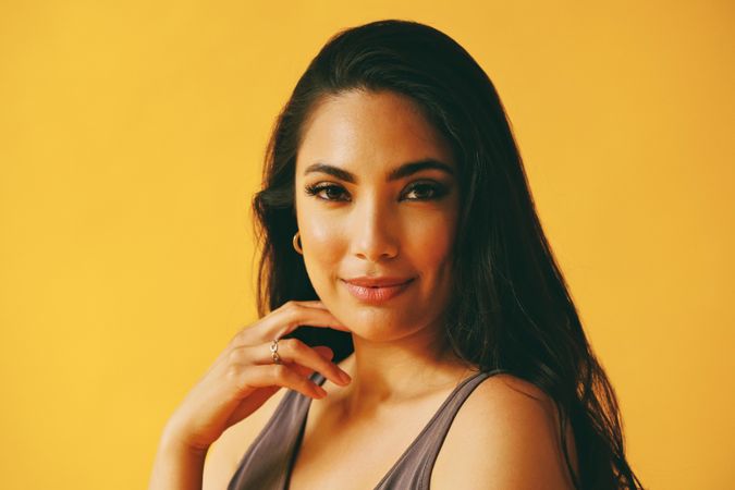 Hispanic woman looking at camera in yellow room with her hand to her chin