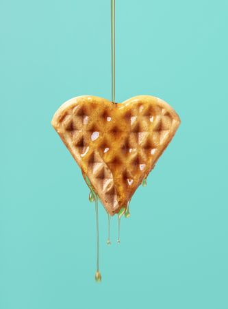 Waffle shaped like a heart with maple syrup isolated on a green background