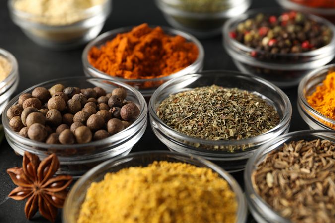 Glass bowls full of spices on dark table, close up