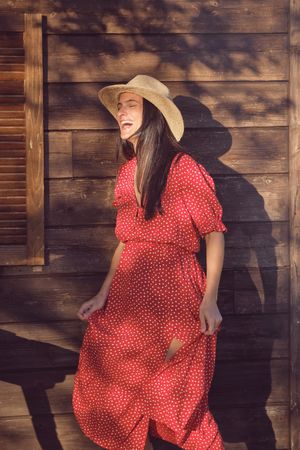 Cheerful female in red dress laughing and dancing near wooden wa