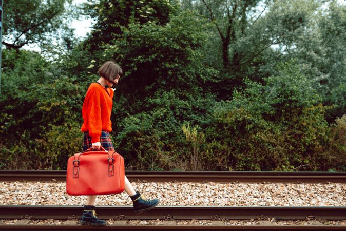 Woman with suitcase walking on railroad ties