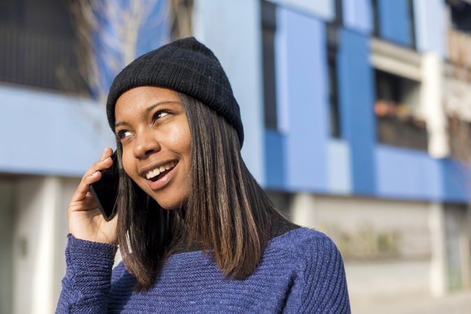 Female in wool hat and blue sweater talking on phone on sunny day with space for text