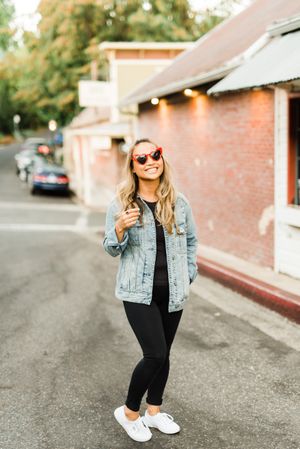 Woman in blue denim jacket standing on sidewalk