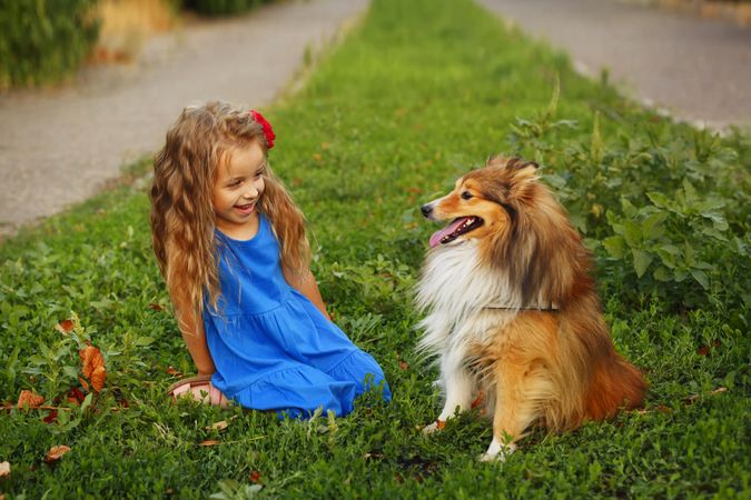 Happy girl in blue dress sitting with dog in the grass