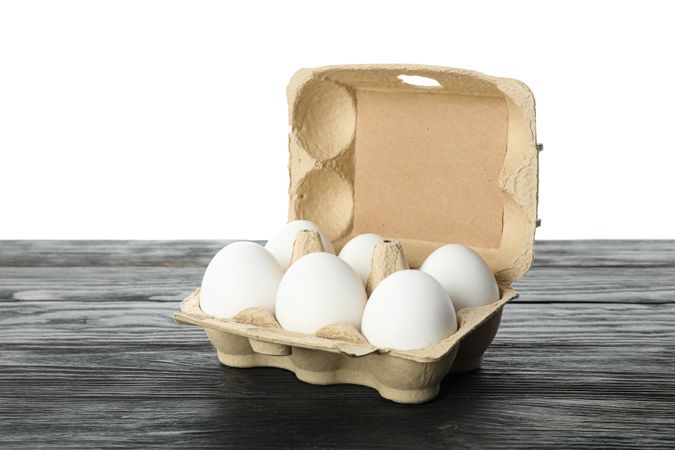 chicken eggs in carton box on wooden table isolated on plain background, space for text