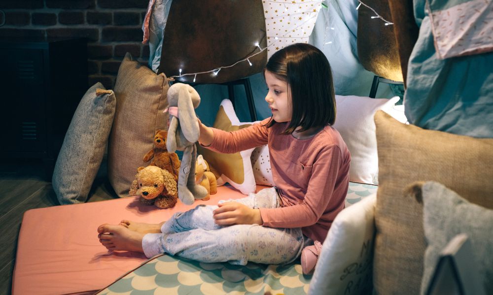 Girl in pajamas playing alone with teddies in a play shelter