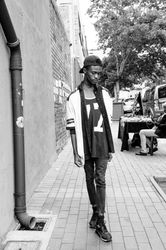 Young man poses on the sidewalk in fashionable clothing looking down