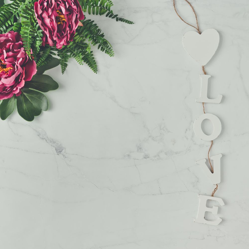 Pink flowers and leaves on marble background with the word “Love”