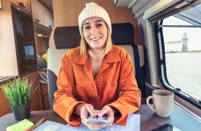 Woman in orange shirt sitting and smiling in van with smartphone