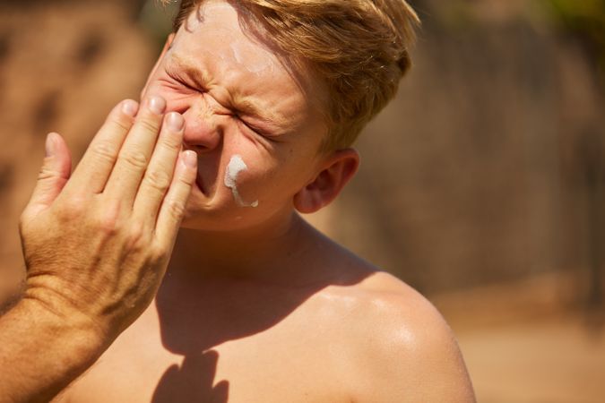 Faceless man applying sun cream on kid