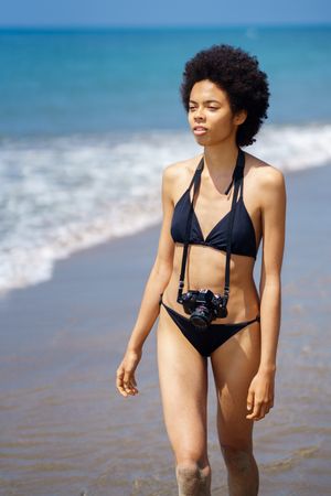 Woman walking along the shore in bikini with camera around her neck