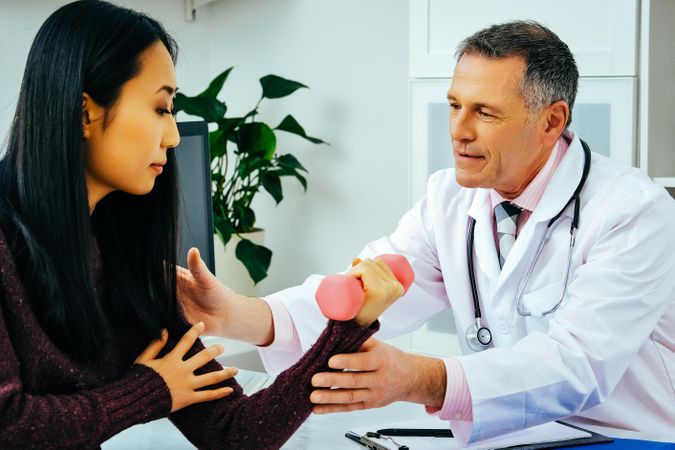 Male doctor with female patient working with dumbell