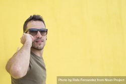 Calm male leaning on yellow wall talking on cell phone 0vpnR4