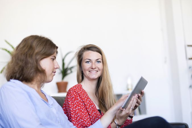 Two females at home sitting on sofa using digital tablet