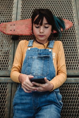 Girl with smartphone and skateboard lying on walkway
