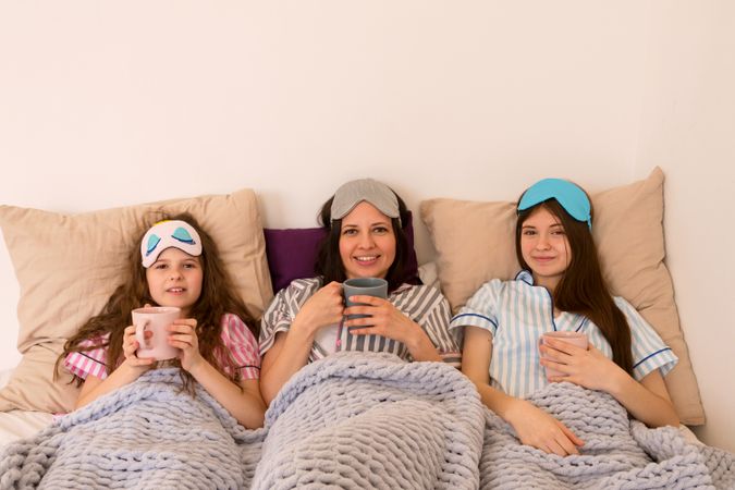 Mother and daughters enjoying morning coffee in bed together.