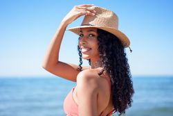 A Joyful Woman Wearing a Beautiful Straw Hat at the Beach, Enjoying the Warm Sunshine