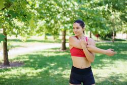 A young woman is in nature, preparing for exercise by stretching outdoors, embracing fitness and enjoying the greenery
