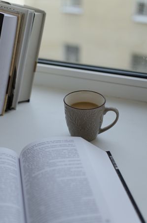 Cup of coffee beside an open book on light table