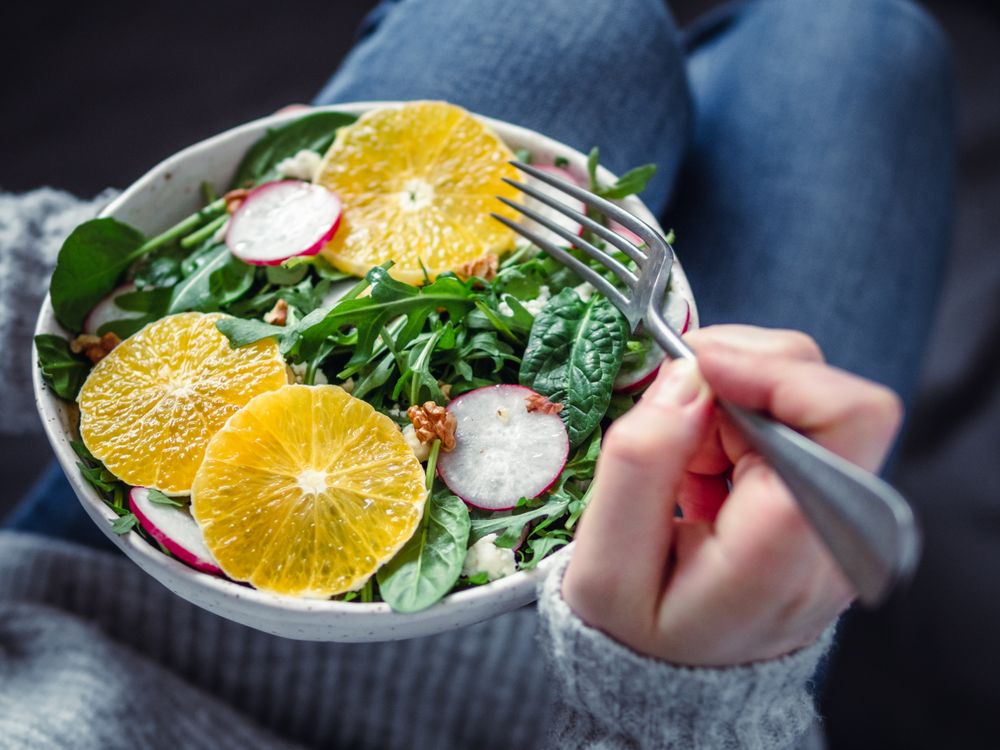 Person eating a salad with arugula, orange and radish
