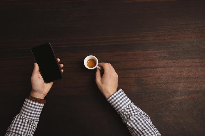 Businessman in plaid shirt checking cell phone with espresso shot