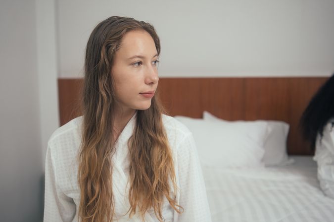 Woman in bathrobe sitting on bed at home