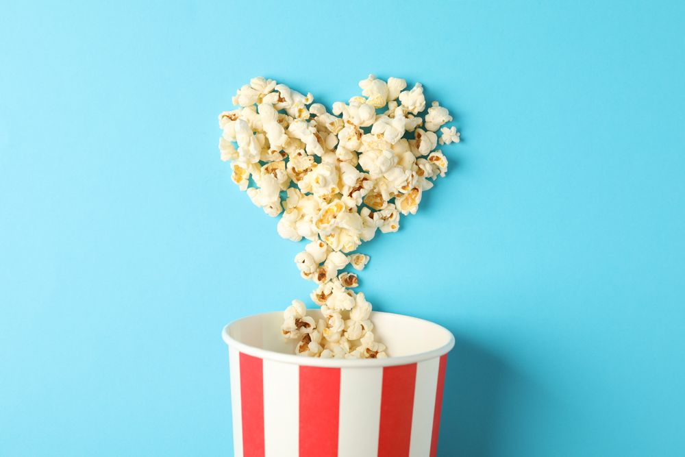 Popcorn heart and striped bucket on blue background, space for text