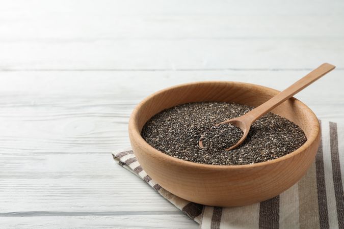 Wooden bowl with chia and spoon on wooden background, space for text