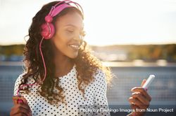 Attractive Black woman in pink headphones smiling at her phone 0voRZ5