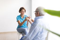 A physiotherapist talks to her patient, an older man, while examining his hand and arm for injuries
