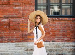Woman outside a building in summer dress and sun hat
