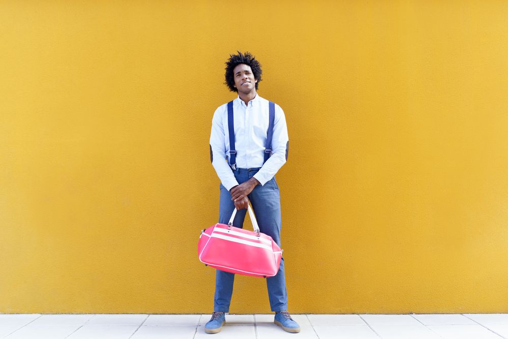 Man standing tall with sports bag standing in front of yellow wall