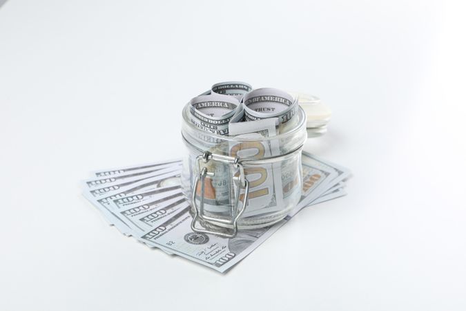 Stacks of American cash money in glass jar on light background