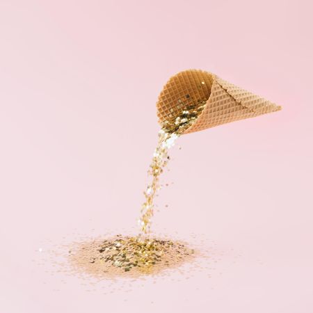 Ice cream cone pouring gold glitter on pastel pink background