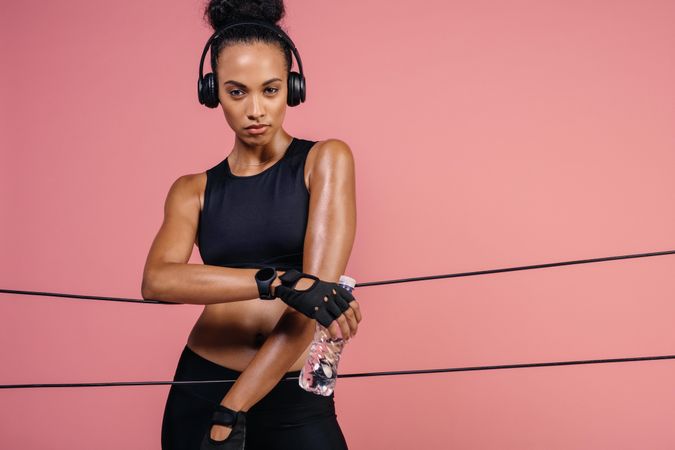 Fitness woman with headphones and water bottle leaning over rubber bands in studio