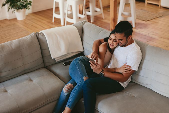 Loving young couple relaxing on sofa and using mobile phone