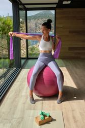 Sporty female sitting on fitness ball and stretching arms in fitness studio