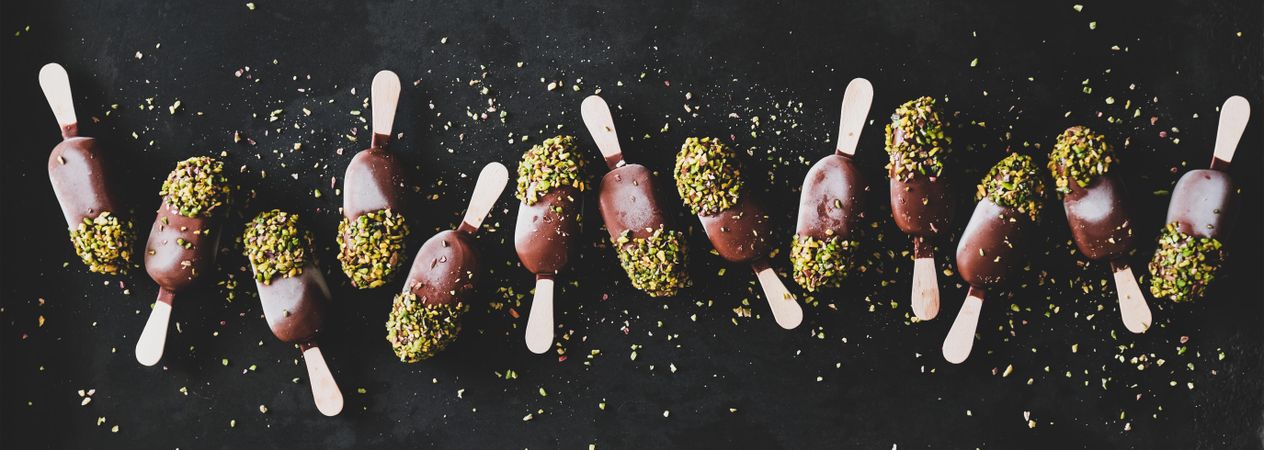 Ice cream chocolate pistachio popsicles, dark background, top view, wide composition