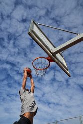 Basketball player throwing ball into hoop against cloudy sky