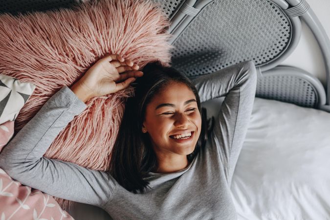 Young woman lying on bed with eyes closed and laughing