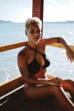 Woman in dark bikini sitting on wooden dock near seashore