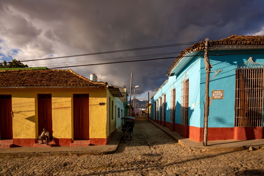 African man sitting on doorstep of yellow building under cloudy sky