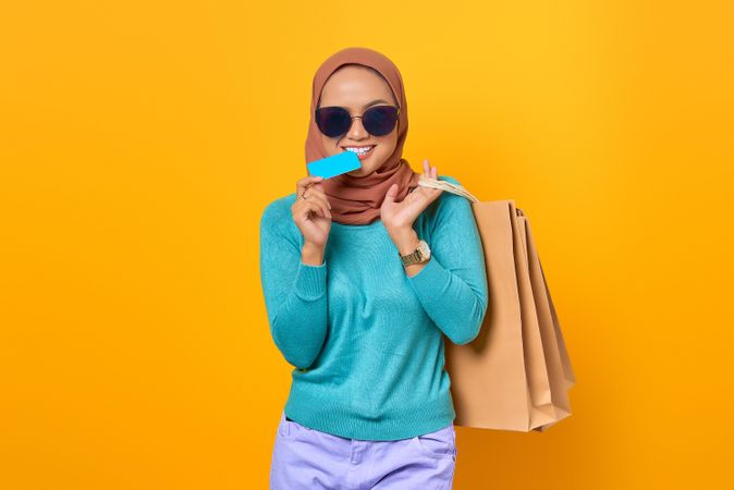 Muslim woman smiling with shopping bags and credit card in her mouth