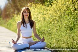 Female wearing light sport clothes meditating on yoga mat on forest path 49rMQb