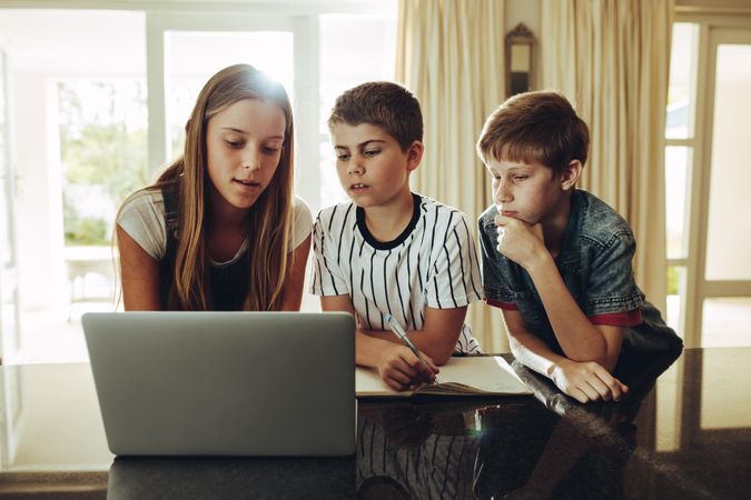 Boys and a girl looking at a laptop at home and learning